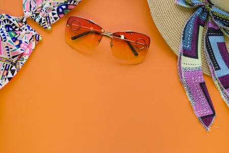 Travel and tourism concept. Summer fashion accessories- a straw hat, a patterned swim suit and pink sunglasses on orange one-color background, top view. Space for a text or product display.の写真素材