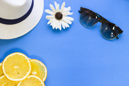 Travel and tourism concept. Blue one-color background with a white hat, sunglasses and orange slices, top view. Space for a text or product display.の写真素材