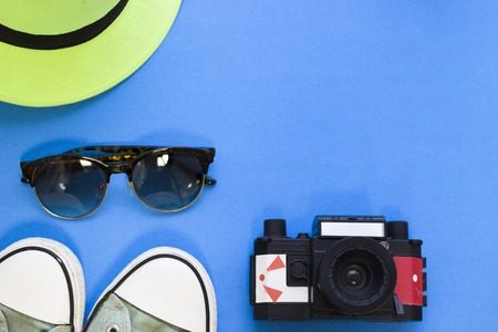 Travel and tourism concept. Blue one-color background with travelling accessories- a camera, sport shoes, sunglasses and a hat, top view. Space for a text or product display.の写真素材