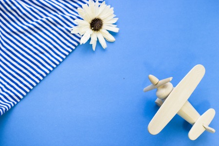 Ready to travel. Blue one-color background with beach striped shirt and wooden airplane, top view. Space for a text or product display.の写真素材