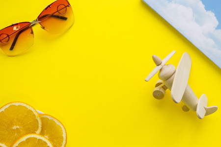Bright yellow one-color background with, sunglasses, wooden airplane and slices of orange, top view. Travel or tourism concept. Space for a text or product display.の写真素材