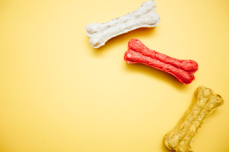 Yellow one-color background with tree colored dog bone snacks, close up, top view. Pet care and veterinary concept. Spase for your text or image.の写真素材