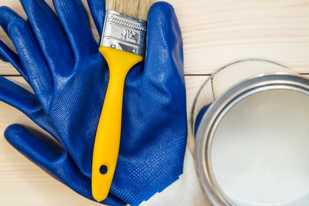 Protection for redecoration work. A pair of blue latex gloves, a brush and a tin can of white oil paint on a light uncolored wooden background. Close up. Top view. Space for your text or pruduct display.の写真素材