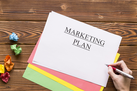 A hand writing marketing plan, a pile of colored paper sheets and balls of crumpled paper. Business and work concept. Space for your text or product display.Top view.の写真素材