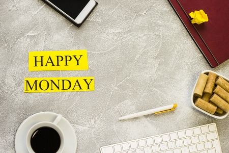 Happy monday inscription printed on a yellow paper with a cup of coffee, keyboard and office items, light concrete background.Business and motivation concept. Space for your text or product display.の写真素材