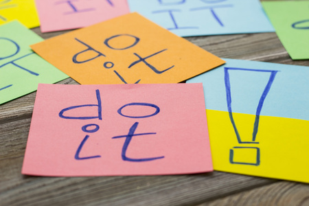 Colorful note papers inscribed with do it words, close up. Light wooden background. Business and...
