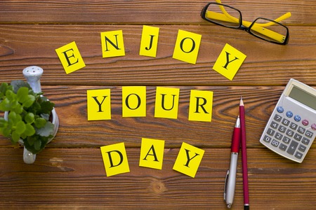 Enjoy your day printed inscription with office supplies on a rustic wooden table, top view. Business...