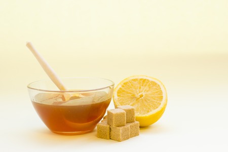 Sugar depilation or skin care essentials- A bowl of honey with a wooden spoon, a fresh lemon and brown sugar cubes on a light background. Spa and body care concept.の写真素材