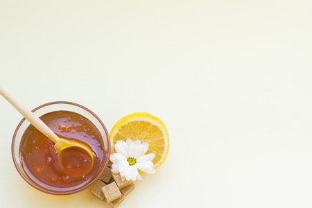 Sugar depilation or skin care background- A bowl of honey with a wooden spoon, a fresh lemon, camomile flower and brown sugar cubes, top view. Spa and body care concept.の写真素材
