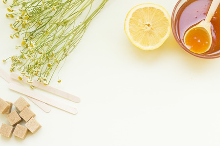 Background with a frame of natural ingredients for beauty and health- a bowl of honey with a wooden spoon, lemon, camomile, brown sugar cubes and wooden sticks. Space for your text or imageの写真素材