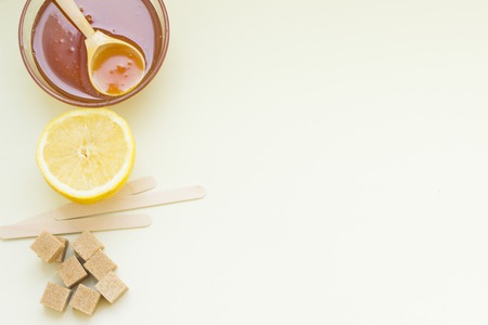 Background with natural ingredients for beauty and health- a bowl of honey with a wooden spoon, lemon, brown sugar cubes and wooden sticks. Space for your text or imageの写真素材