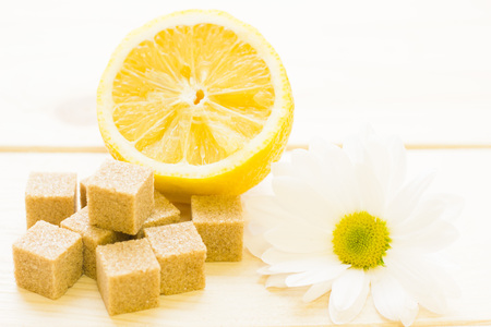 Concept for medical care, spa, beauty procedures, healthy diet, cooking, bevarages.A close up of brown sugar cubes, white flower and a half of a lemon, light wooden background.の写真素材