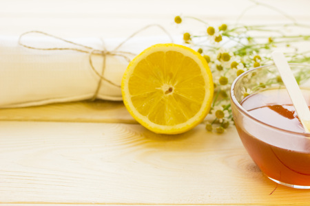 Spa therapy background.A bowl of honey, camomile flowers, lemon and a towel. Light wooden background. A space for your text or product display.の写真素材