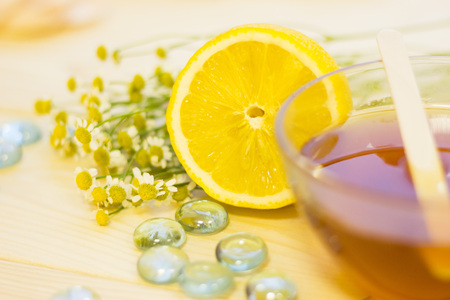 Beauty and spa essentials- a lemon, a bowl of honey, camomile flowers and blue glass stone pebbles. Close up. A space for your text or product display.の写真素材