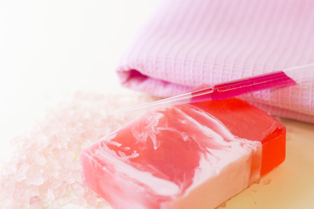 Beauty, spa, make up concept. A bar of homemade rose soap, an oil dropper on a table with scattered salth grains. Space for your text or product display.の写真素材