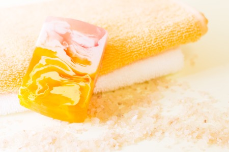 Spa resort or cosmetics banner. A pile of folded towels, a colorful bar of handmade soap and bath salt grains on the table, close up. Space for a text or product display.の写真素材