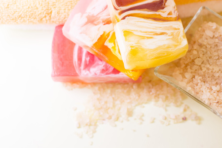 Spa, massage, bath accessories, aromatherapy concept.Three bars of colorful fruit soap, a bowl of bath salt and towels, top view. Space for a text or product display.の写真素材