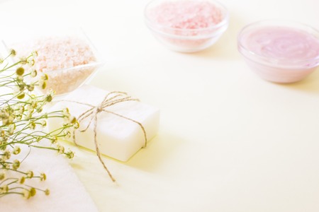 Spa resort background with bath essentials- a bar of homemade vanilla soap, camomile flowers and bowls with bath salt and body lotion unfocused. Space for your text or product display.の写真素材