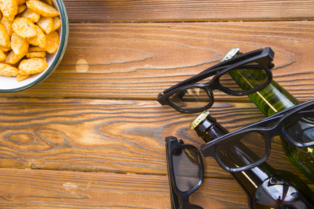 Relax and enjoy a movie with friends. Weekend, hobby and leisure concept. Bowl with bread crumbs, two bottles of beer and three pairs of glasses on a rustic wooden table. Close upの写真素材