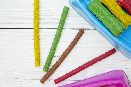 Pet care, veterinary concept. Training and feeding a dog. Colorful dog snacks- sticks and bones in plastic bowls and lying on the table. White wooden background. Space for a text or imageの写真素材