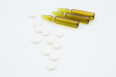 Veterinary and animal healthcare background. Curing pets. Three ampouls of dark green glass and white oval pills on a white background, close up. Space for your text or image.の写真素材