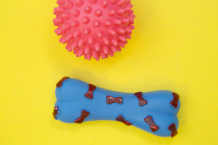 Little pet friend having fun. A pink rubber squeaky ball and a bleu rubber bone on a yellow background, close up.の写真素材