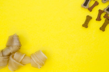 Pet food and pet care concept. A one-color yellow background with chewing dog bone snacks and dry dog food, close up. Top view. Space for your text or image.の写真素材