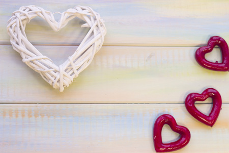 Light colored wooden background with a white rattan woven heart and red hearts. Top view. Space for your inscription or product display. St. Valentine's, anniversary, wedding, mother's day concept.の写真素材