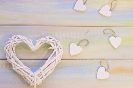 Light colored wooden background with a white rattan woven heart wreath and wooden hearts. Top view. St. Valentine's, anniversary, wedding, mother's day concept.の写真素材