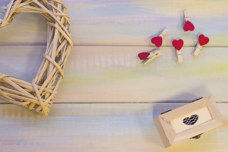 Natural wicker wreath in a shape of heart, a wooden box and heart-pins on a light backgound. Top...