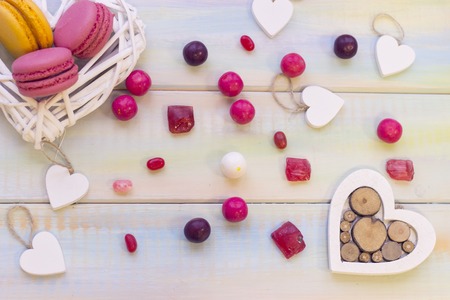 A white woven heart wreath with macaroons, wooden hearts and colorful candies scattered on the table. Space for your text or image on the left. St. Valentines, anniversary, wedding concept.の写真素材