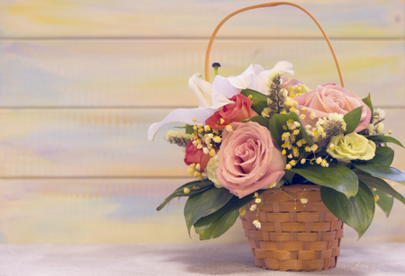 A flower basket with frangrant lilies, red and pink roses against light colored wooden background. Space for a text or image. St. Valentine's, anniversary, wedding concept.の写真素材