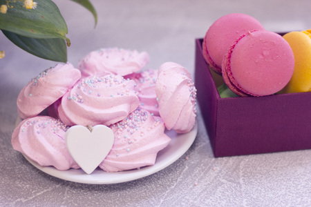 A plate with pink marshmallows with a wooden heart and a box of delicious macaroons. St. Valentines, anniversary, wedding concept with copy space. Space for your text or product display.の写真素材