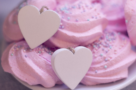 A close up of a plate with pink marshmallows and two wooden hearts. A light festive dessert. St. Valentines, anniversary, wedding concept with copy space. Space for your text or product display.の写真素材