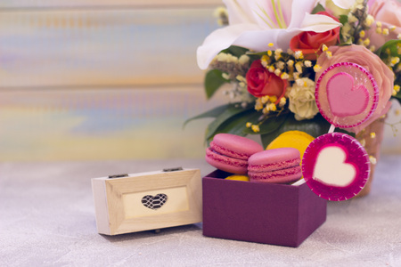 Romantic festive compositions with flower basket, a box of macaroons, lolipop with hearts and a wooden casket with a gift. Light colored wooden background.St. Valentines, anniversary, wedding conceptの写真素材