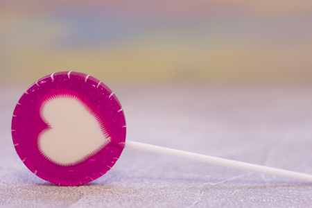 Blurred background with a lolipop with a heart image in a close up. St. Valentines, anniversary, wedding concept with copy space. Space for your text or product display.の写真素材