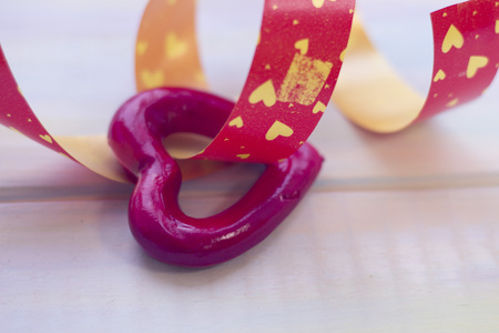 A red heart on a red ribbon with hearts in a close up. Light wooden background. St. Valentines, anniversary, wedding concept with copy space. Space for your text or product display.の写真素材