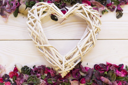 A woven heart on a light wooden background with borders of floral petals and leaves, top view. Concept of St.Valentine's Day, anniversary, weddingの写真素材