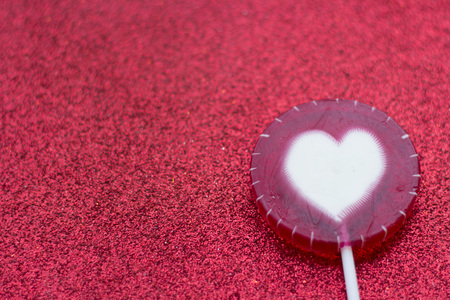 Valentine's concept with a lolipop candy with a heart glitter red background, close upの写真素材