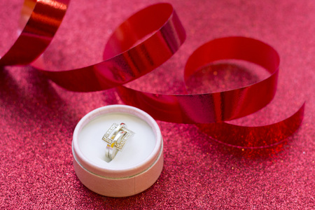 Valentine's concept with a golden ring in a pink round box glitter red background, close up