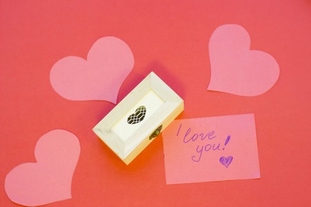 The concept of St.Valentine's Day with a love note and paper hearts, red background top view