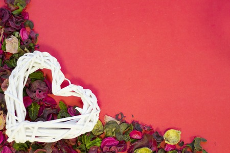 The concept of St.Valentine's Day with a woven heart, red background with a corner of rose petals and leaves top view, copy spaceの写真素材