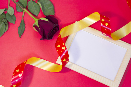 The concept of St.Valentine's Day with a beautiful red rose and wooden photo frame, red background, top viewの写真素材
