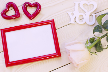 Concept of St.Valentine's Day, Love, Anniversary, Wedding with a pale cream rose, I love you inscription and a red photo frame, natural wooden background, top viewの写真素材
