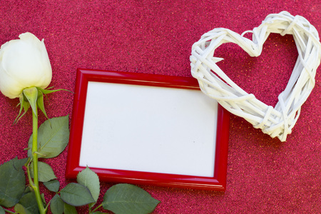 The concept of Love, Wedding, Anniversary, Gift. A romantic surprise with a beautiful pale cream rose and a red photo frame, glitter red background, top viewの写真素材