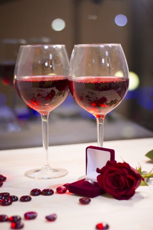 The concept of Love, Wedding, Proposal, Anniversary. A romantic evening with two glasses of red wine, a wedding ring in a box and a beautiful red velvet rose. Dark blurred backgroundの写真素材