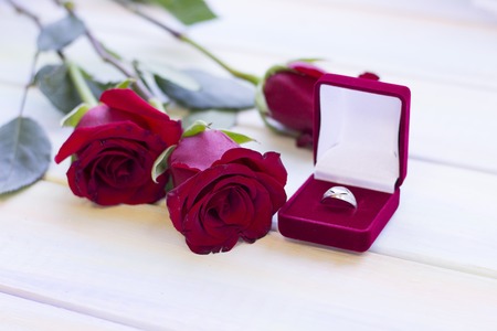 The concept of Love, Wedding, Proposal, Anniversary, St. Valentine's Day, Mother's Day with beautiful red roses and a wedding ring in a red velvet box in a close up, light wooden backgroundの写真素材