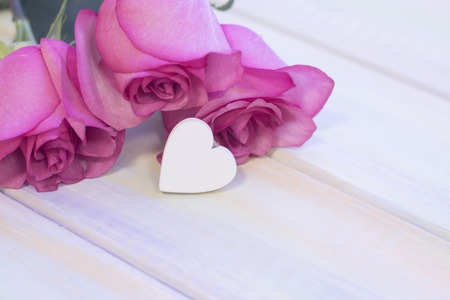 The concept of Love, Wedding, Proposal, Anniversary, St. Valentine's Day, Mother's Day with beautiful pink roses and a decorative wooden heart on a light wooden tableの写真素材