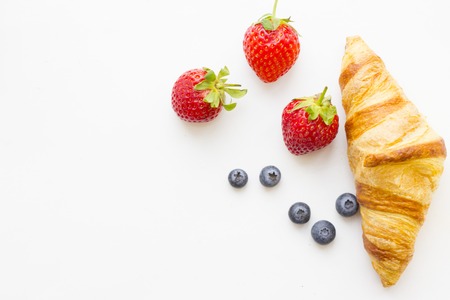 Healthy Breakfast Concept with a fresh buttery croissant, blueberries and strawberries on white, top view, copy spaceの写真素材