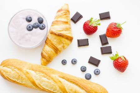 Healthy Breakfast Concept: fresh croissant, fench baguette, youghurt, blueberries, strawberries and chocolate on white, top view mock upの写真素材